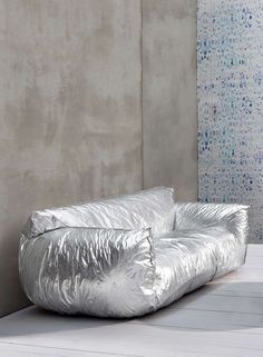 two shiny silver pillows sitting on top of a white table next to a gray wall