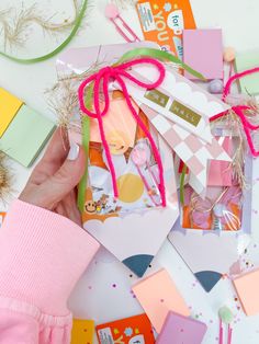 a person is holding up some cards with pink and green ribbons on them next to other items