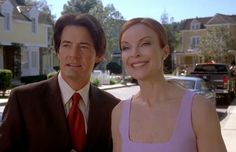 a man and woman standing next to each other in front of some houses on the street