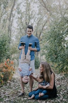 a man and two women are playing with their child in the woods while another woman looks on