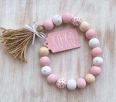 a pink and white beaded bracelet with a tassel on the end that says oxox