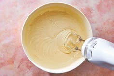 an electric mixer mixing batter in a white bowl on a pink marble counter top,