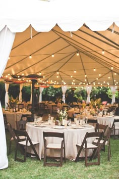 an outdoor tent with tables and chairs set up for a wedding reception in the grass