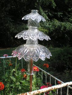 a glass bird bath sitting on top of a wooden pole in front of some flowers