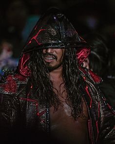 a man with long hair wearing a black hat and leather jacket at a concert in the dark