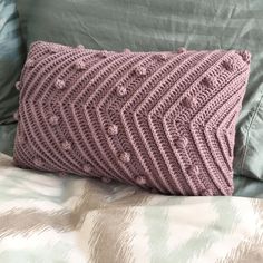 a crocheted pillow sitting on top of a bed next to a green comforter