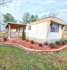 a mobile home sits in the middle of a grassy area with trees and shrubs around it