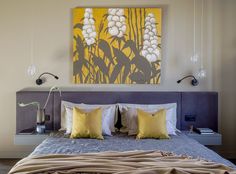 a bed with yellow and white pillows in a bedroom next to a painting on the wall