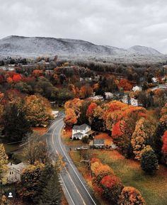 an aerial view of a road surrounded by trees with fall foliage on the mountains in the background