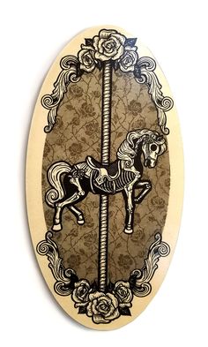 an oval wooden plaque with a horse on it's side and roses around the edges