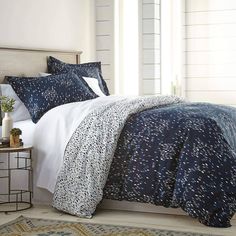 a bed with blue and white comforters in a room next to a table on the floor