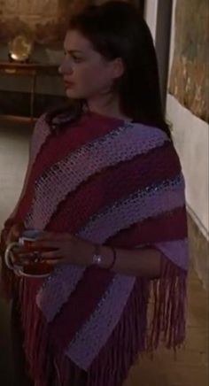 a woman wearing a red and purple shawl holding a cup in her hand while standing next to a wall