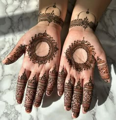 two hands with henna tattoos on them, one is circular and the other is round