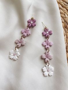 purple and white flowers are hanging from gold earwires on a white fabric background