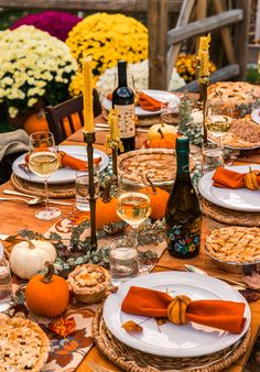 an outdoor table set for thanksgiving dinner with wine, crackers, and pumpkins