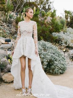 a woman standing in front of some bushes wearing a dress with high low hems