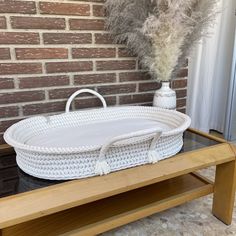 a white wicker basket sitting on top of a wooden table next to a brick wall