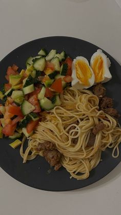 a black plate topped with pasta, meat and veggies next to an egg