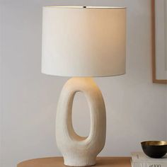 a white table lamp sitting on top of a wooden table next to a black bowl