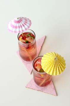 two glasses filled with drinks sitting on top of pink napkins next to an umbrella