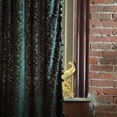 the curtain is open in front of a brick wall with a gold statue on it