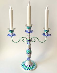 three white candles with blue and green designs are on a candle holder in the shape of a candelabra