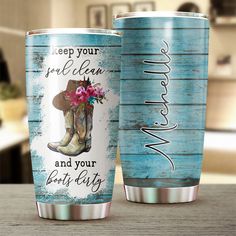 two travel mugs with cowboy boots and flowers on them sitting on a wooden table