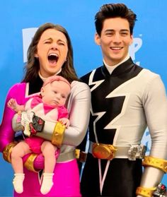 a man and woman holding a baby in front of a blue background