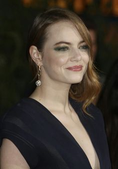 a woman in a black dress with green eyeshadow and gold earrings smiling at the camera