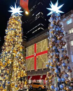 two christmas trees in the middle of a city street with lights and decorations on them