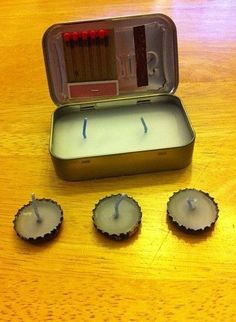 an open tin with three candles in it on top of a wooden table next to other items