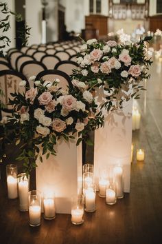 flowers and candles are arranged on the floor in front of white vases with greenery