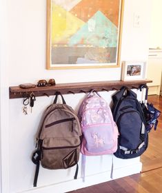 three backpacks are hanging on a wall near a painting and two framed pictures in the background