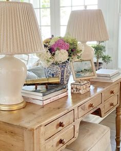 two lamps are sitting on a table with books and flowers in vases next to them