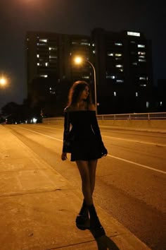 a woman is walking down the street at night with her hand on her hip and looking off into the distance