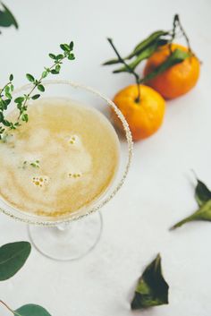 an orange cocktail with garnish in a wine glass next to two oranges