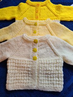 three knitted sweaters sitting next to each other on a blue blanket with yellow buttons