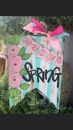 a wooden sign that says spring with flowers on it and a pink bow hanging from the top