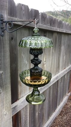 a glass bird feeder hanging from a wooden fence