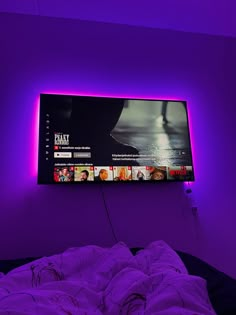 a flat screen tv mounted on the wall above a bed in a purple lit room