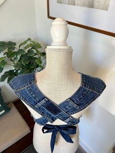 a white mannequin with a blue jean jacket on it's chest and a potted plant in the background