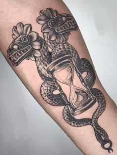 a tattoo with an hourglass, snake and flowers on the arm that is black and white