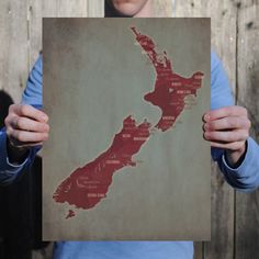 a person holding up a poster with the map of new zealand in it's hands