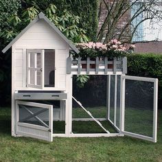 a white chicken coop with flowers growing on it's roof and two doors open