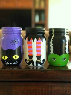 three painted mason jars sitting on top of a wooden table