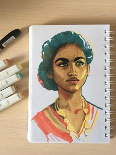 a drawing of a woman's face on a notebook next to crayons