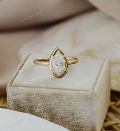 a gold ring with a pear shaped diamond in it sitting on top of a box