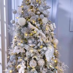 a white christmas tree decorated with silver and gold ornaments, snowflakes and lights