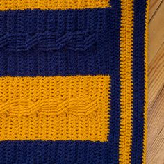 a crocheted blanket with yellow and blue stripes on the bottom is laying on a wooden floor