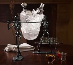 skeleton figurines are sitting in an ice bucket with bottles and glasses on the table